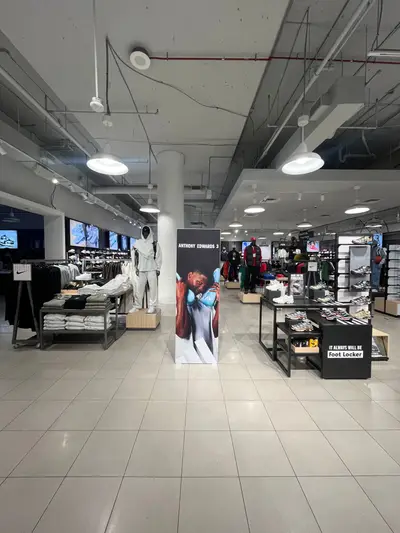 Wide view of a Foot Locker store interior showing an Anthony Edwards 3 freestanding display surrounded by Nike apparel and sneaker displays.