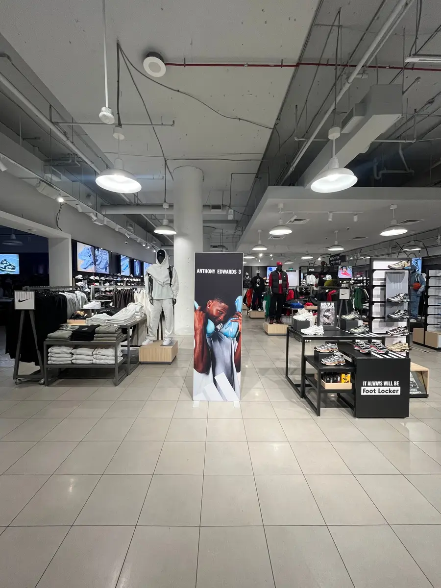 Wide view of a Foot Locker store interior showing an Anthony Edwards 3 freestanding display surrounded by Nike apparel and sneaker displays.