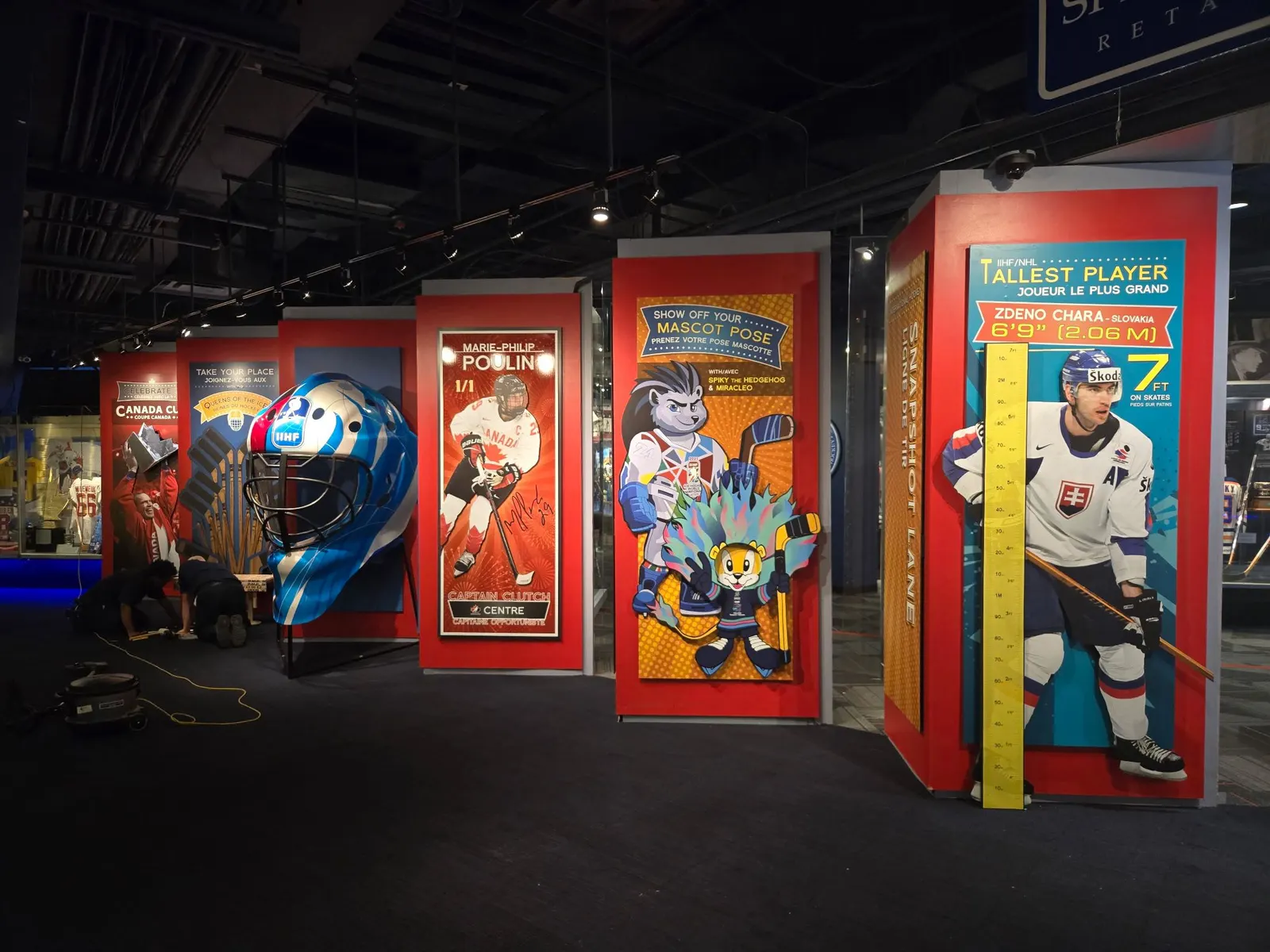 An IIHF international hockey interactive exhibit is shown mid-installation, featuring oversized props and player displays.