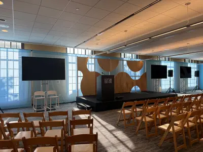A DotDev2026 conference stage features wooden backdrop panels with circular cutouts, a black podium, and display screens on either side.