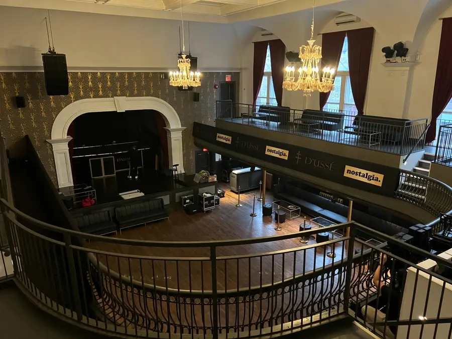 An overhead view of an elegant multi-level event venue shows chandeliers, balcony seating, and D'USSÉ and Nostalgia branded signage.