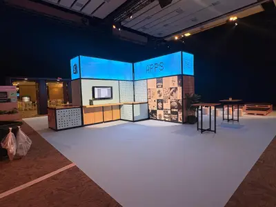 A corner trade show booth for Shopify Apps and DotDev features blue illuminated light box signage and pegboard display walls.
