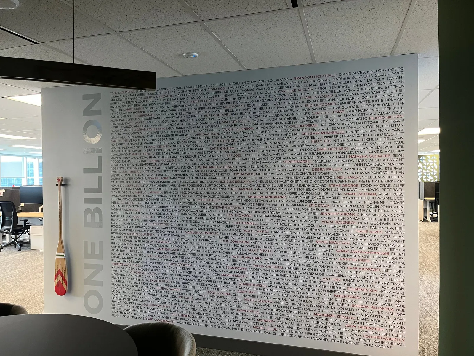 A close-up of an office wall mural shows hundreds of employee names arranged in a repeating pattern to mark a one billion achievement milestone.