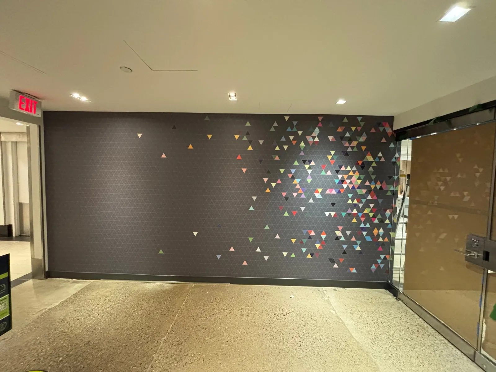 A large-format dark accent wall displays a multicolored triangle pattern that transitions from a dense cluster to a sparse scatter near the entrance doors.