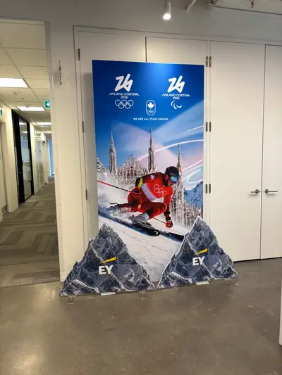 A Milano Cortina 2026 Team Canada branded banner displayed alongside mountain cutouts in an office corridor.