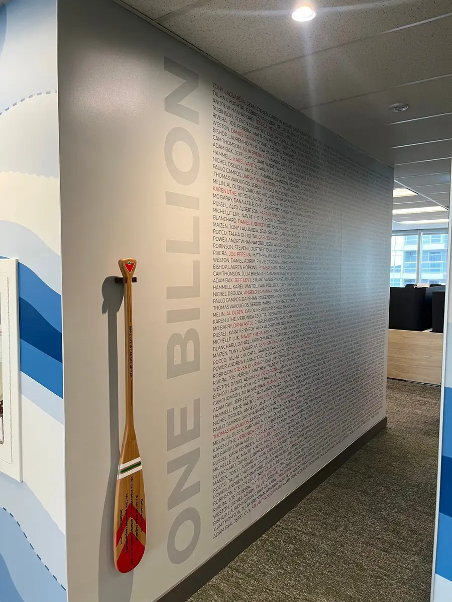 A corner office wall features a One Billion name mural alongside a mounted ceremonial wooden paddle with Canadian imagery.