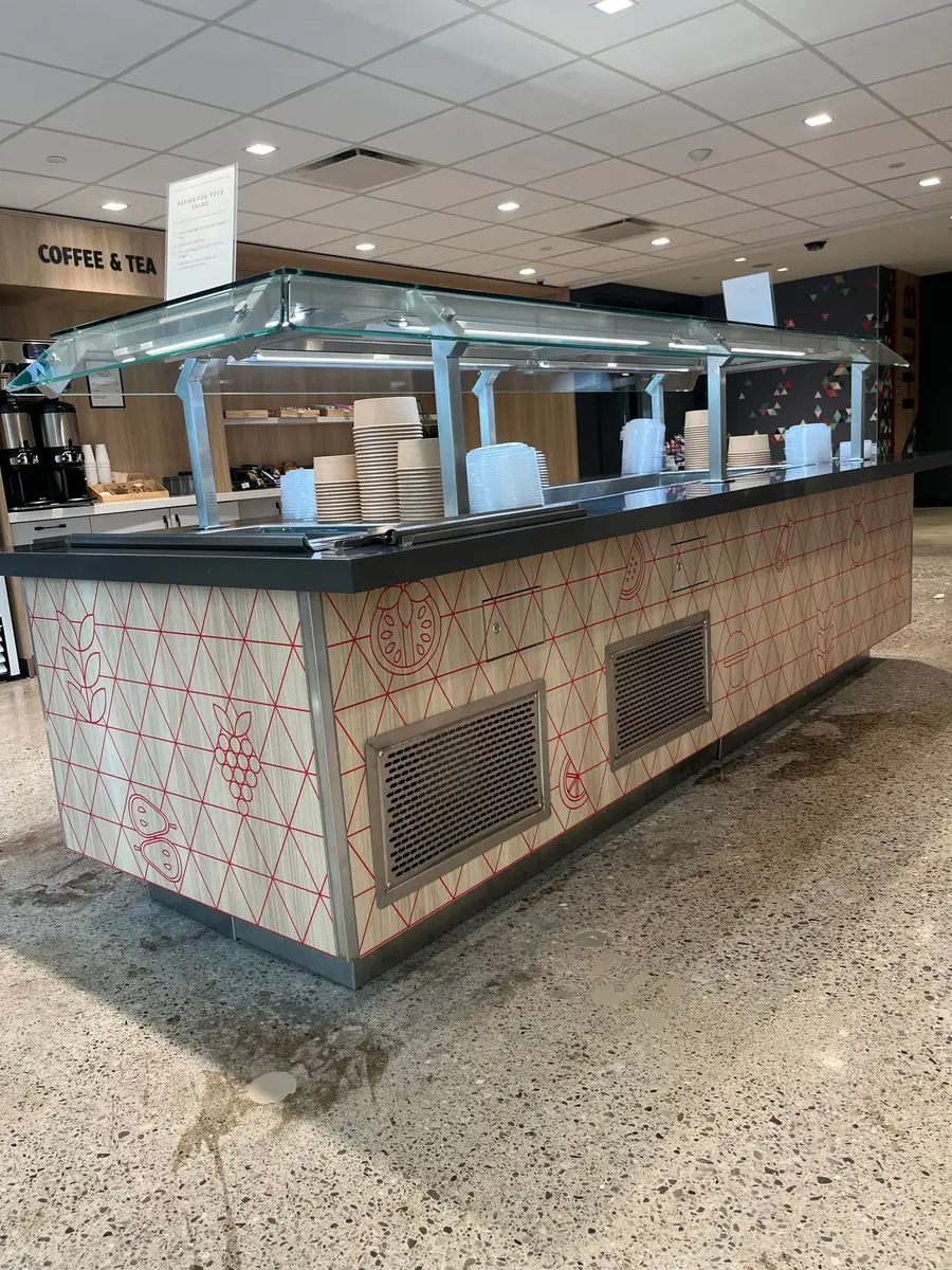 The opposite side of a salad bar island displays a full-length decorative panel wrap featuring red botanical illustrations and ventilation grilles.
