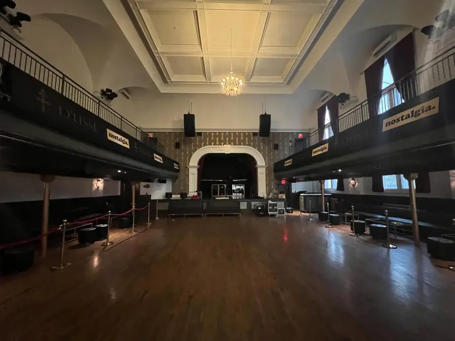 A wide-angle floor-level view of a grand ballroom shows hardwood floors, a mezzanine level, and branded sponsor banners displayed throughout the space.