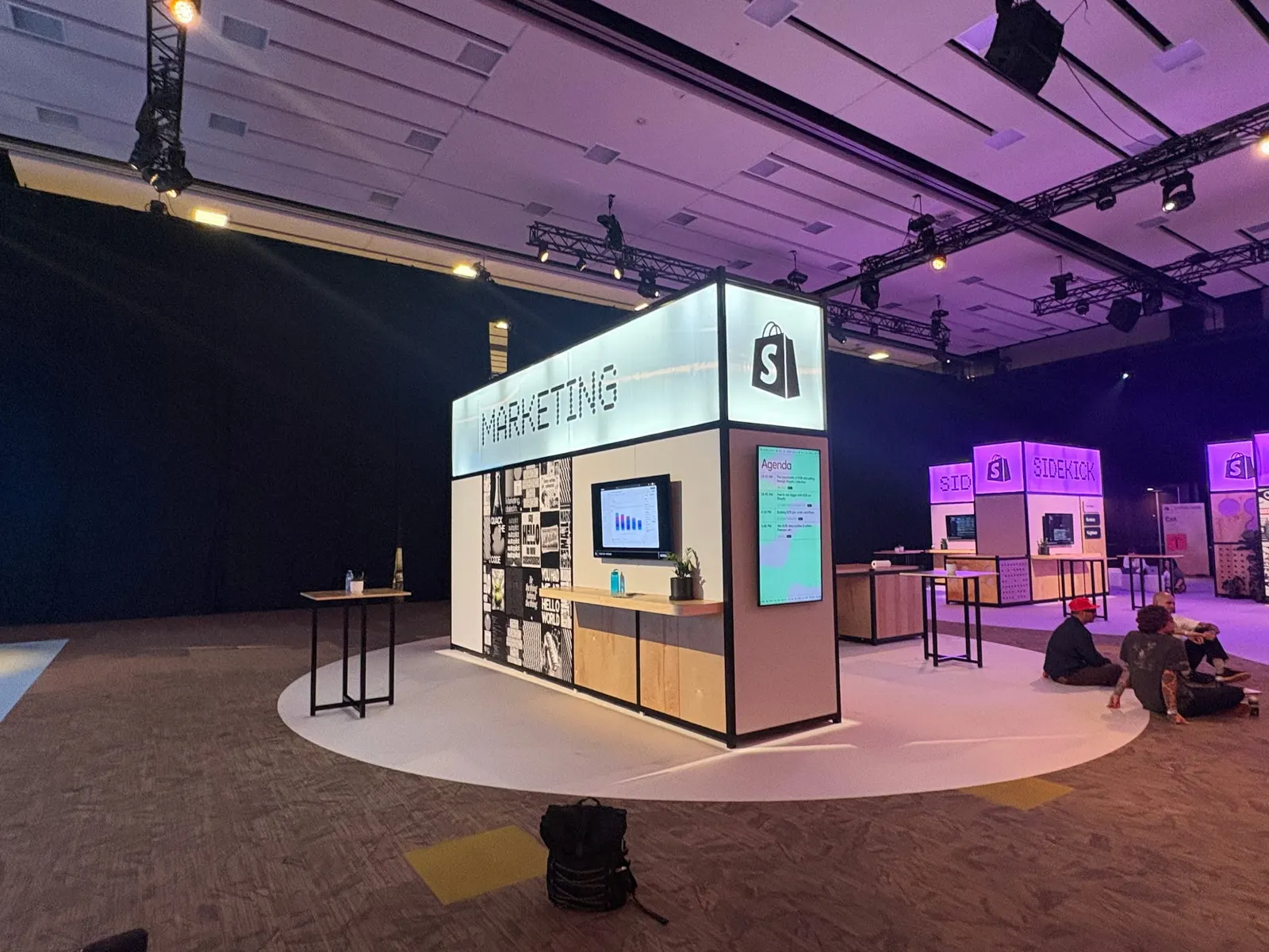A Shopify Marketing booth displays illuminated signage and display screens inside a dark event hall.
