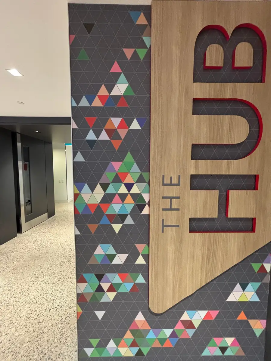 A close-up of The Hub entrance pillar shows a colorful geometric triangle wallcovering and dimensional wood lettering signage.