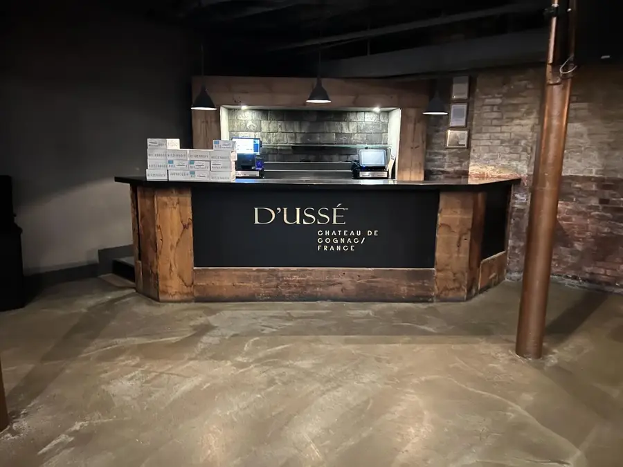 A D'USSÉ Cognac branded bar counter with rustic wood trim and a stone backdrop is shown in a basement-level space.