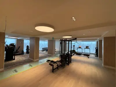A hotel fitness centre under construction featuring cable machines, cardio equipment, and backlit forest mural panels installed on the walls.