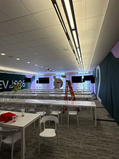 A conference breakout room with white tables and chairs is being arranged with screens and a DotDev2026 branded backdrop.