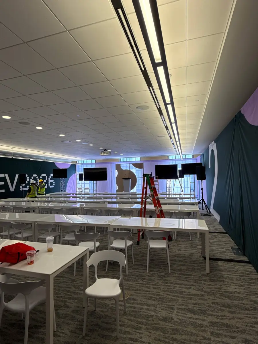 A conference breakout room with white tables and chairs is being arranged with screens and a DotDev2026 branded backdrop.